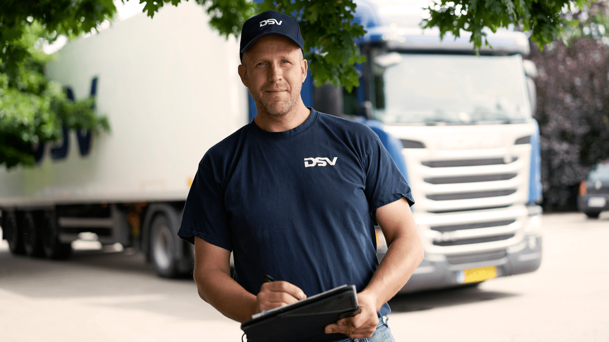 DSV-medarbeider med en skriveplate står foran en lastebil.